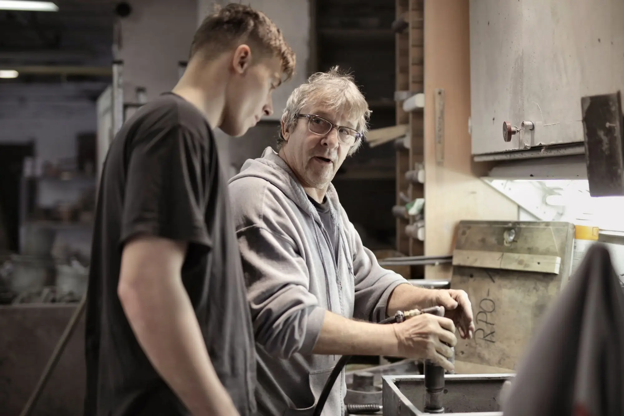 Experienced tradesman showing a young apprentice how to use a tool at a workshop bench